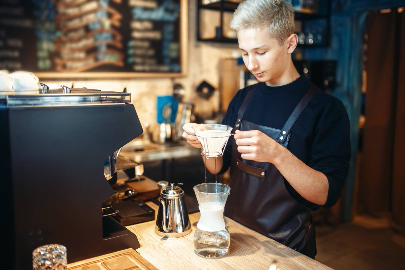 Young male barista makes coffee at the counter